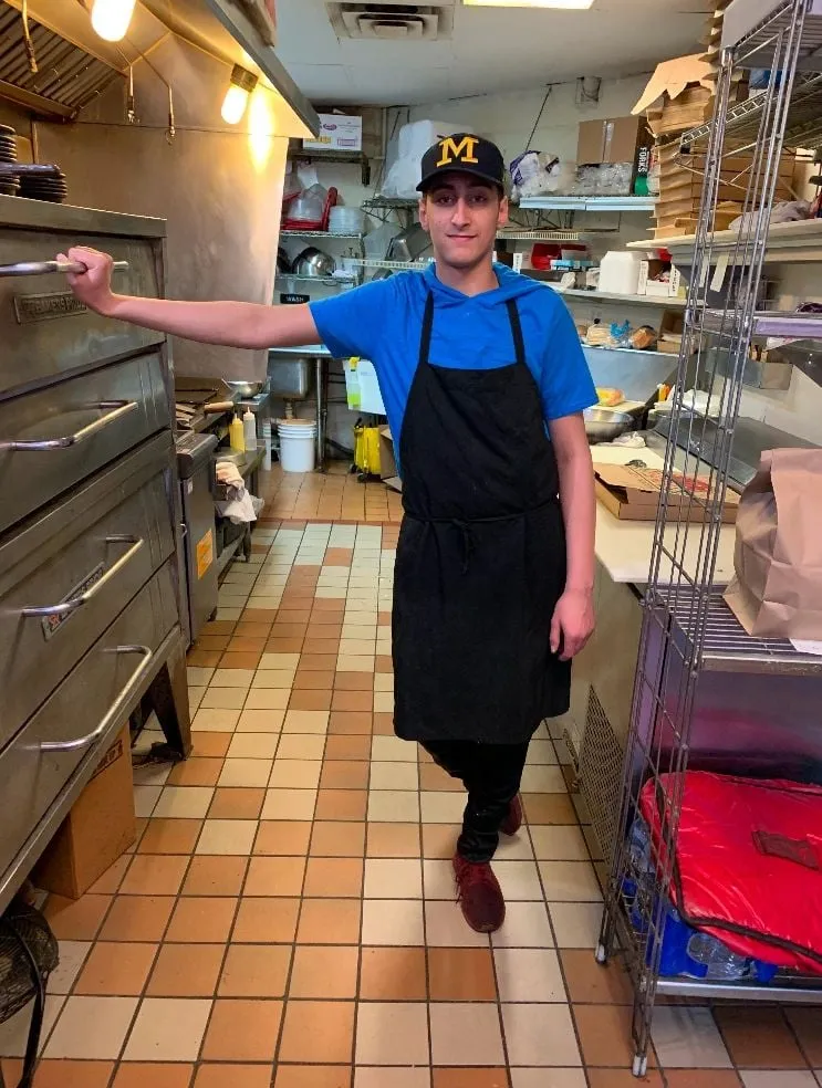 Team member in an apron leaning on the pizza oven